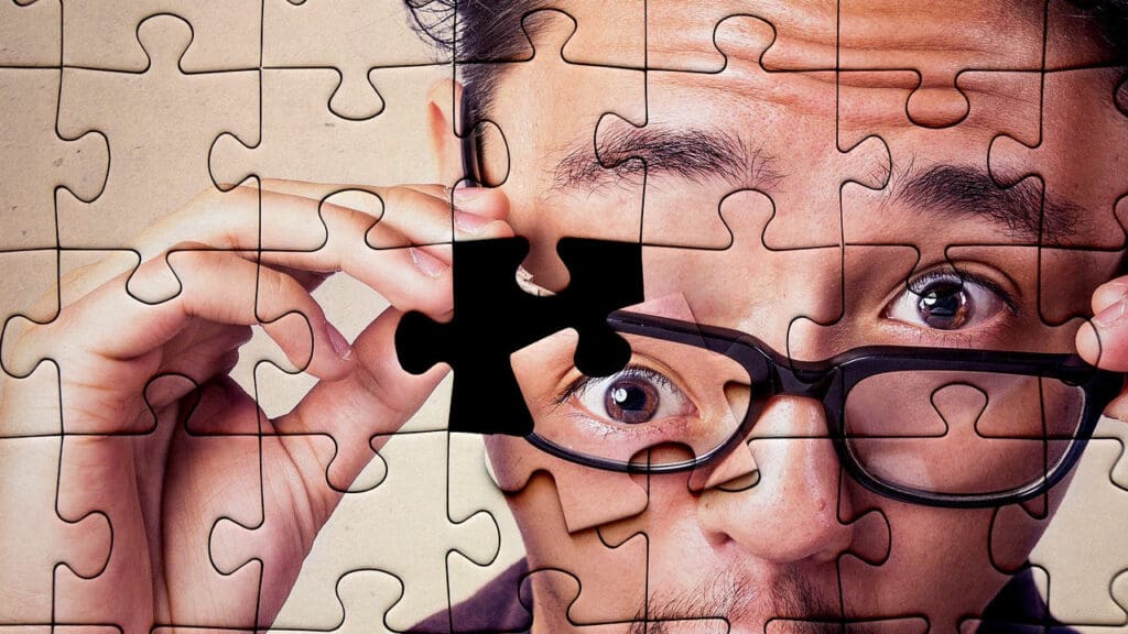 jigsaw puzzle of man wearing glasses with one piece remaining to be placed. The missing piece is his eye